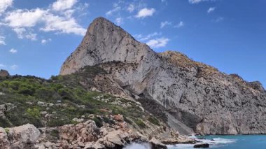 A breathtaking view of a towering rock formation situated by the sparkling sea, beautifully surrounded by lush greenery