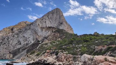 The breathtaking view of a towering rock formation alongside a serene seascape, all under a clear blue sky