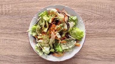 Canlı bir salata. İçinde taze yeşillikler, doğranmış havuçlar ve kırsal bir kasede servis edilen soslar var.