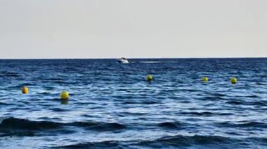 Sakin ve sakin bir okyanus manzarası canlı sarı şamandıralar arasında sakin sularda süzülen bir tekneyi gösteriyor.