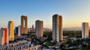 Günbatımında modern binaların yer aldığı güzel bir gökyüzü. Canlı renkler ve yeşil alanlar sergileniyor..