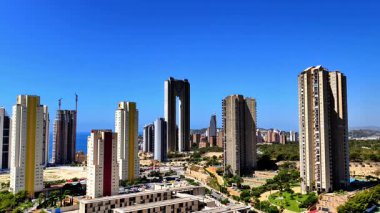 Açık mavi gökyüzüne karşı gökdelenleri gösteren canlı bir şehir siluetinin nefes kesici manzarası.