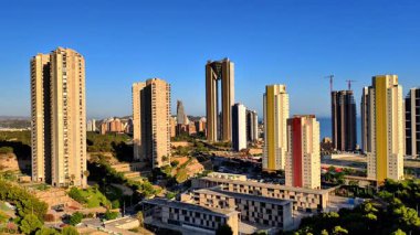 Gökdelenlerin ve açık mavi gökyüzünün altında yemyeşil yemyeşil olduğu modern bir şehrin çarpıcı manzarası..