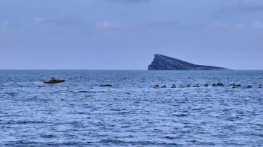 Kayakçılar, sakin denizin tadını çıkarırken, bir adanın nefes kesen uzak arkaplanına eşlik ediyorlar.