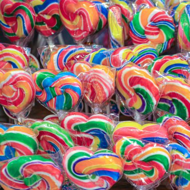 Kalbinde ve yuvarlak şekillerde şeffaf plastiğe sarılı gökkuşağı lolipoplarının yatay çekimi. Parlak ve renkli şekerler, eğlence, kutlama, parti, çocuklar ve bayram teması için ideal..