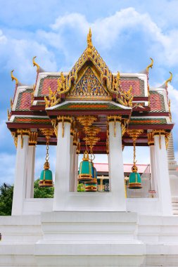 Bangkok, Tayland 'daki Wat Rakhang tapınağında süslü bir pavyon. Altın Tayland motifleri, kırmızı çatı detayları, ve tavanın altında asılı büyük pastel mavi çanlar, beyaz sütunlar ve mavi gökyüzü tarafından çerçevelenmiş.