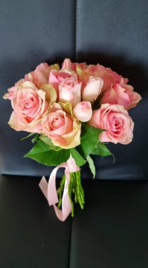 Siyah bir sandalyede pembe kurdeleli bir buket narin gül, çiçekçi konsepti.