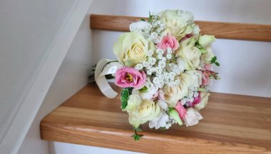 Pembe ve beyaz gül renginde yuvarlak düğün buketi, Eustoma, gypôila ve yeşillik. Tahta merdivenlerde bir buket..
