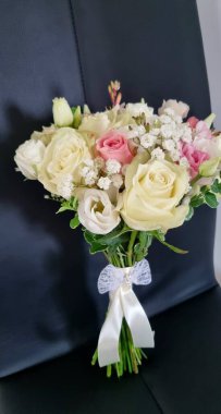 Düğün buketi masanın üstünde. Yuvarlak, narin bir düğün buketi, pembe ve beyaz renkli güller, Eustoma, çigila ve siyah bir sandalyede yeşillik.. 