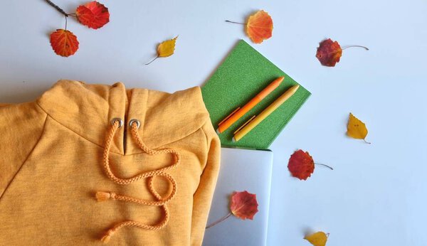 Осенняя тема исследования с оранжевой толстовкой, ноутбуком, блокнотом и ручками, осенние листья на белом фоне. Предпосылки для обучения или бизнеса в осеннее время.