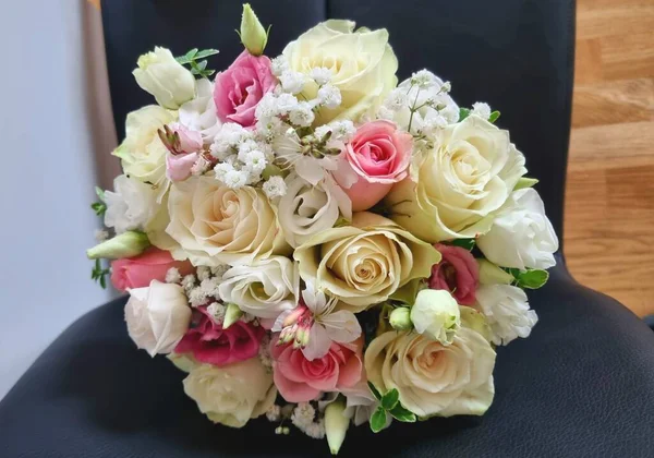 Yuvarlak, narin bir düğün buketi, sapları ve çiçekli pembe ve beyaz gül renginde, Eustoma, gypthe ve yeşillik siyah bir sandalyede..