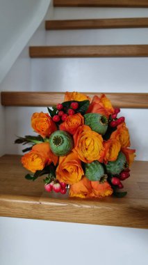 Sonbaharda yuvarlak bir buket portakal gülleri, hiperikum, gelincik ve yeşillik tahta merdivenlerde.