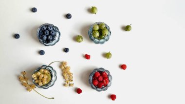 Düzgün beslenme ve diyet kavramı, ahududu, frenk üzümü, yabanmersini ve bektaşi üzümlü mavi cam vazolar beyaz arka planda..