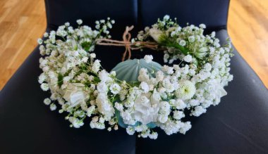 Kafasında beyaz çingeneden yapılmış bir çelenk, kafasında siyah bir sandalye ve mavi bir dekorun arka planına karşı narin bir süs.