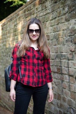 Genç kız, parkta poz arka plan bir tuğla duvar