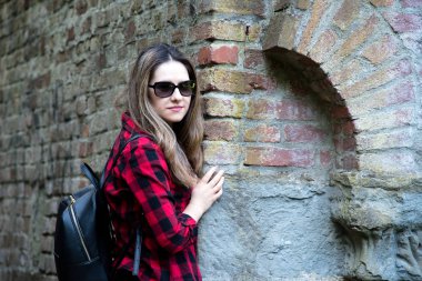 Genç kız, parkta poz arka plan bir tuğla duvar