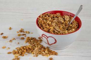 İki kalp ile beyaz bir kase Beyaz ahşap masa üzerinde bir kaşıkla üzerine granola dolu kavrulmuş