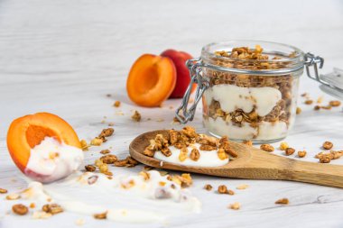 Granola ve yoğurt, tahta kaşık whit granola ve kayısı Beyaz ahşap masa üzerinde dolu bir kavanoz