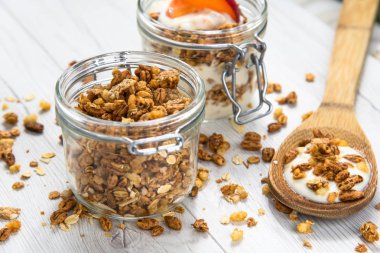 Granola ve yoğurt ve bir kavanoz dolu granola ile ile dolu bir kavanoz Beyaz ahşap masa üstünde tahta kaşık whit granola