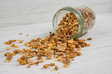 Beyaz ahşap masa üzerinde devrik granola dolu kavanoz