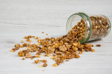 Beyaz ahşap masa üzerinde devrik granola dolu kavanoz