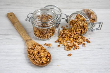 İki granola ve beyaz ahşap masa üzerinde bir tahta kaşık tam whit granola dolu kavanozları