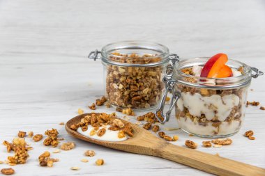 Granola ve yoğurt, tahta kaşık whit granola ve kayısı Beyaz ahşap masa üzerinde dolu bir kavanoz