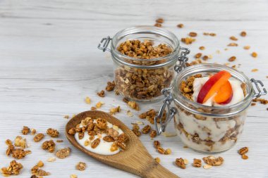 Granola ve yoğurt, tahta kaşık whit granola ve kayısı Beyaz ahşap masa üzerinde dolu bir kavanoz