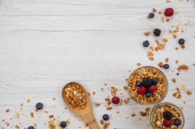 İki granola ve taze meyveler ve tahta kaşık tam whit granola Beyaz ahşap masa, arka plan, üstten görünüm, kopya alanı ile kavanozlar