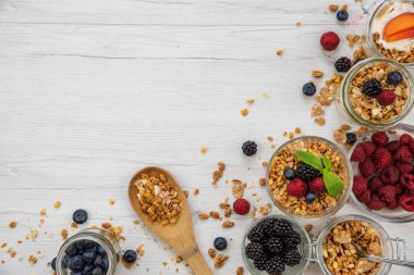 Kavanoz granola, yoğurt ve taze meyveleri ve tahta kaşık tam whit granola Beyaz ahşap masa, arka plan, üstten görünüm, kopya alanı ile tam
