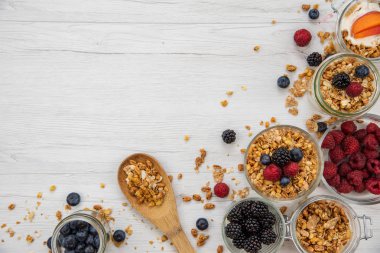 Kavanoz granola, yoğurt ve taze meyveleri ve tahta kaşık tam whit granola Beyaz ahşap masa, arka plan, üstten görünüm, kopya alanı ile tam