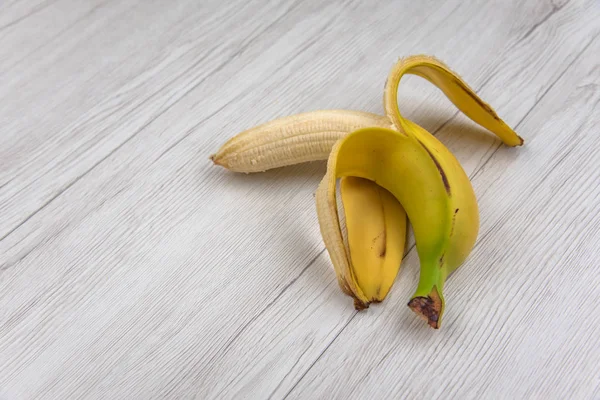 Half peeled banana, open banana isolated on a white wood table.