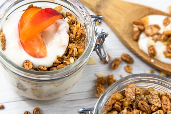 Granola ve yoğurt ve bir kavanoz dolu granola ile ile dolu bir kavanoz Beyaz ahşap masa üstünde tahta kaşık whit granola