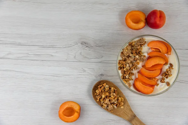 Kayısı yoğurt ve bir tahta kaşık granola bir beyaz ahşap masa, üstten görünüm, kopya alanı dolu dolu bir kase