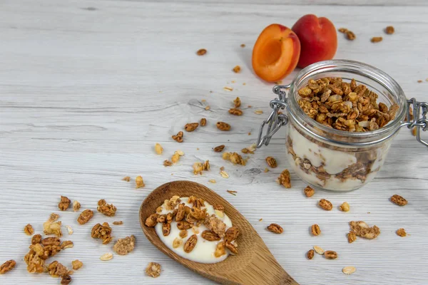 Granola ve yoğurt, tahta kaşık whit granola ve kayısı Beyaz ahşap masa üzerinde dolu bir kavanoz