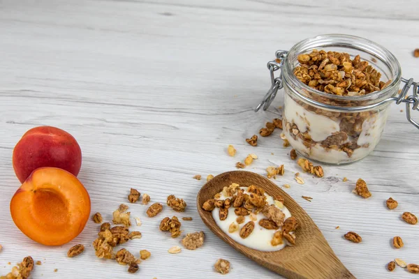Granola ve yoğurt, tahta kaşık whit granola ve kayısı Beyaz ahşap masa üzerinde dolu bir kavanoz