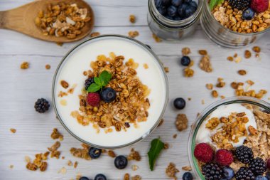 Kavanoz granola, yoğurt ve taze meyveleri ve tahta kaşık tam whit granola Beyaz ahşap masa, üstten görünüm, seçici odak ile tam