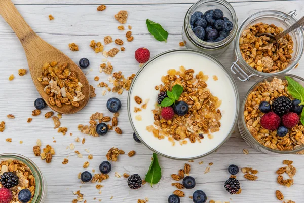 Kavanoz granola, yoğurt ve taze meyveleri ve tahta kaşık tam whit granola Beyaz ahşap masa, üstten görünüm, seçici odak ile tam