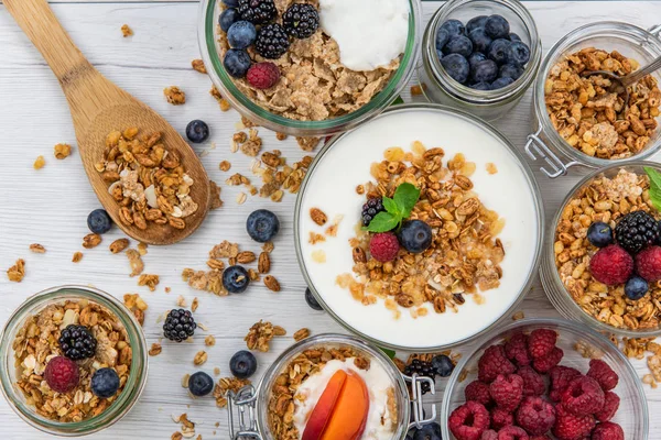Kavanoz granola, yoğurt ve taze meyveleri ve tahta kaşık tam whit granola Beyaz ahşap masa, üstten görünüm, seçici odak ile tam
