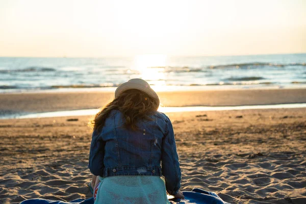 Hayran ve deniz esinti zevk kumsalda güneş doğarken oturan bir kız