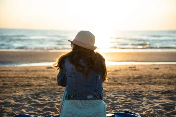 Hayran ve deniz esinti zevk kumsalda güneş doğarken oturan bir kız