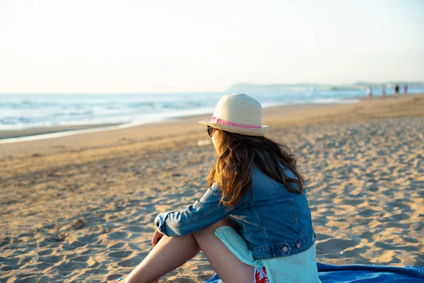 Hayran ve deniz esinti zevk kumsalda güneş doğarken oturan bir kız