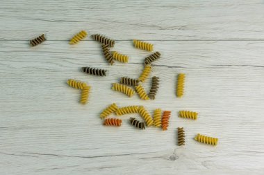 Çiğ çiğ üç renkli düdük durum buğday makarna ıspanak ve beyaz ahşap masa üzerinde domates ile.
