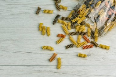 Çiğ çiğ üç renkli düdük durum buğday makarna ıspanak ve beyaz ahşap masa üzerinde domates ile.