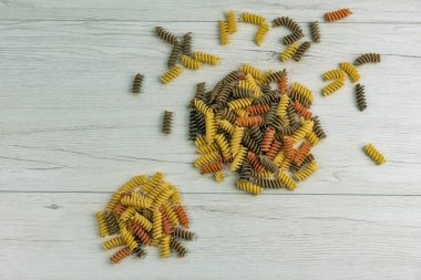 Çiğ çiğ üç renkli düdük durum buğday makarna ıspanak ve beyaz ahşap masa üzerinde domates ile.