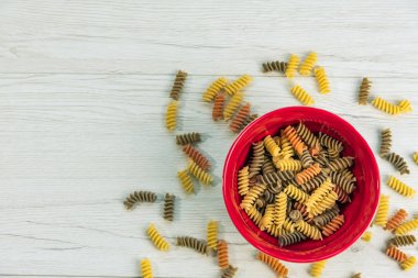Çiğ çiğ üç renkli düdük durum buğday makarna ıspanak ve domates ile ben Beyaz ahşap masa, üstten görünüm üzerinde kırmızı bir kase.