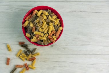 Çiğ çiğ üç renkli düdük durum buğday makarna ıspanak ve beyaz ahşap masa, üstten görünüm üzerinde bir cam kavanoza domates ile.