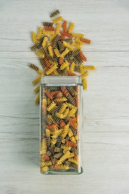 Çiğ çiğ üç renkli düdük durum buğday makarna ıspanak ve beyaz ahşap masa, üstten görünüm üzerinde bir cam kavanoza domates ile.