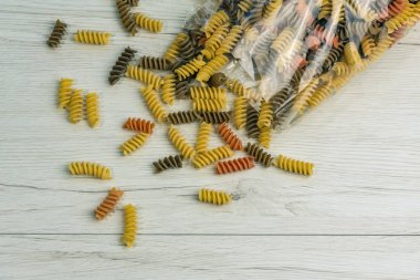 Çiğ çiğ üç renkli düdük durum buğday makarna ıspanak ve beyaz ahşap masa üzerinde domates ile.