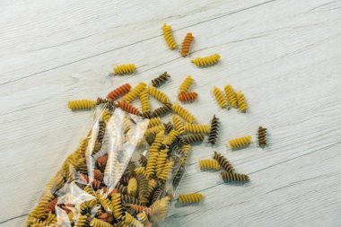 Çiğ çiğ üç renkli düdük durum buğday makarna ıspanak ve beyaz ahşap masa üzerinde domates ile.